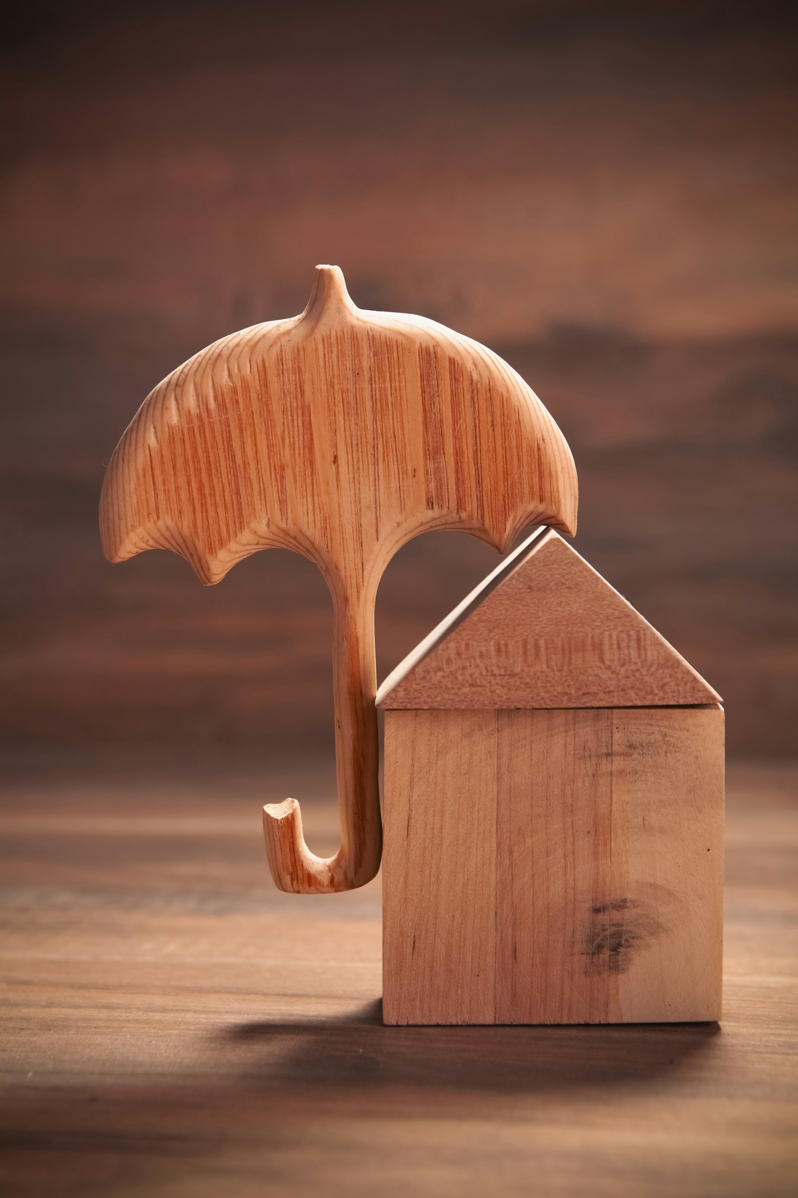 A small wooden umbrella protecting a wooden house figurine on a wooden surface — the visual metaphor for short-term rental insurance shielding your investment from risk